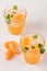 Mandarin cocktail with ice and mint in beautiful glasses and jug, fresh ripe citrus on white wooden background. Sweet orange juice