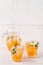 Mandarin cocktail with ice and mint in beautiful glasses and jug, fresh ripe citrus on white wooden background. Sweet orange juice