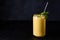 Mango lassi in glass with tube on dark background