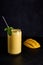 Mango lassi in glass with tube on dark background