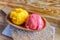 Mango and raspberry fruit sorbet scoops in a wooden dish on a platter sprinkled with icing sugar on a wooden table