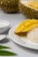 Mango sticky rice with pandan leaves, coconut milk and sugar against blurry durian fruits background