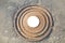Manhole cast iron heavy brown with a pattern of several rings on the background of concrete screed. In the center of the round whi