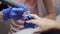 Manicure master in blue gloves polishes client nail in salon