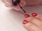 Manicure master paints the nails of the client. Manicurist with a brush paint your nails in red.