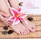 Manicured female bare feet with pink lily flower and spa stones over bamboo mat