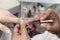 A manicurist applies a deep red gel coat nail polish onto the index fingernail of a female customer. Manicure procedure at a salon