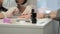 Manicurist master is applying pink gel on client nails in salon, hands closeup.