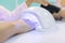 Manicurist uses an ultraviolet lamp for fixing gel nail polish. Nail and hand care in beauty salon.