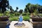 A manmade concrete stream in the center of a park surrounded by lush green trees and plants and colorful flowers