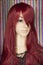 Mannequin with bright long red hair and black lace top posing on blurry colorful beads background