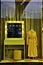 Mannequin wears a long yellow female dress, next to a lighted mirror resting on a make-up desk, all yellow to match the dress.