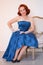 Mannered beautiful vintage woman dressed in blue retro dress sitting on a chair alone and smiling on white background