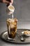 Mans Hand Pours Milk Into Glass of Iced Coffee