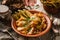 Mans hand sprinkles dill on fried potatoes with bacon and pickles on rustic wooden background, close up