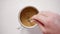 Mans hand stirring coffee with milk in white metal cup on white table