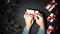 Mans hands wrap a gift. Black background of Xmas adorned with baubles and lights