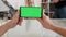 Mans point of view holding a smartphone horizontally with green screen on