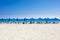 Many beach chairs and umbrellas on white sand sea beach with a blue sky.