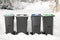 Many black recycling bins on snow outdoors. Winter season