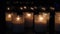 Many candles mysteriously burn in front of the window in complete darkness, blurred reflections and lights of lamps in the glass,