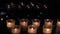 Many candles mysteriously burn in front of the window in complete darkness, blurred reflections and lights of lamps in the glass,