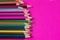 Many colored pencils lie on a pink background. Copy spase. The concept of back to school, the educational process, study at school