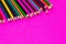 Many colored pencils lie on a pink background. Copy spase. The concept of back to school, the educational process, study at school