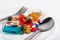 Many colored pills, capsules, syringe and bottle in a dish with a spoon and a fork.