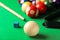 Many colorful billiard balls, cue and chalk on green table, closeup
