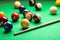 Many colorful billiard balls and cue on green table