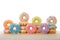 Many colorful candy coated donuts on a light wood table isolated