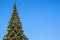 Many decorations and garland on a huge artificial Christmas tree outdoors on a blue sky background. At sunny summer day