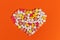 Many different pills and tablets folded in shape of heart on orange background.