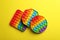 Many different rainbow pop it fidget toys on yellow background, flat lay