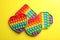 Many different rainbow pop it fidget toys on yellow, flat lay