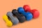 Many dumbbells of different colors, stand in a row according to weight seniority, on a colored background, concept