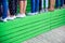 Many female legs in various shoes stand in line on a wooden green tribune