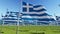 Many flags of Greece waving on wind in green field.