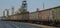 Many freight cars of the train stand next to large silos