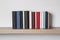 Many hardcover books on wooden shelf near white wall