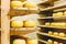 Many heads of yellow Dutch cheese in wax ripen on wooden shelves in a cheese factory. Small craft manufacturing business cheese.