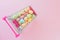 many multi-colored miniature artificial eggs in a miniature food cart on a pink background. Easter sale concept