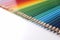 Many multicolored pencils lying in color of rainbow on white background closeup