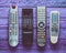 Many obsolete TV remotes on a violet rustic wooden table. Top view.