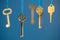 Many old keys of yellow gold color are hanging on thread on a blue background. The concept of the selection of access or password