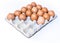 Many orange spotted brown eggs in carton open box container on white backdrop. View from the top