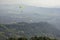 Many paragliders on bright colored parachutes fly over the city in a foggy mountain valley aerial view