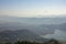 Many paragliders on bright multicolored parachutes fly over the city near the lake in a foggy mountain valley aerial view