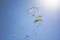 A many paragliders on colorful parachutes in a clear blue sky with bright sunshine